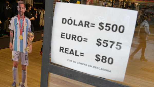 A sign with exchange currency values of the unofficial so-called "Blue Dollar" of the parallel "blue" market, is displayed in the window of a store in Buenos Aires near a cardboard figure of Argentine football star Lionel Messi, on April 26, 2023. Argentina's government on April 25, 2023, accused the country's rightwing opposition of fueling a dramatic erosion of the peso against the US dollar, and ordered an investigation. The slide started last week after several days of pressure on the peso in a period of pre-election uncertainty in a country with exchange controls in place to try to limit the effects of a financial crisis and rampant inflation. (Photo by Juan MABROMATA / AFP) Argentina ditches US dollar for imports from China
