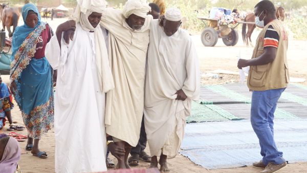 رجلان يساعدان لاجئًا سودانيًا مسنًا عبر الحدود إلى تشاد في مخيم في الكفرون 