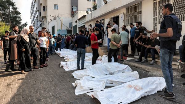People stand by the bodies of victims of Israeli air strikes outside the morgue of al-Shifa hospital in Gaza City on October 12, 2023 as raging battles between Israel and the Hamas movement continue for the sixth consecutive day. (Photo by MOHAMMED ABED / AFP) Gaza