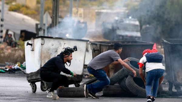 Palestinian youths take cover behind rubbish containers during confrontations with Israeli troops at the northern entrance of the West Bank city of Ramallah near the Israeli settlement of Beit El on October 27, 2023, as battles continue between Israel and the Palestinian Hamas group. (Photo by Jaafar ASHTIYEH / AFP) West Bank