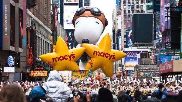 Snoopy balloon floats in the air during the annual Macy's Thanksgiving Day parade along Avenue of Americas with the Radio Music Hall in the background. (Gary 718/ Shutterstock)