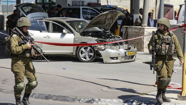 Members of the Israeli security forces walk in front of a damaged car at the Qalandia checkpoint near Jerusalem, following a suspected ramming attack on September 21, 2023. (Photo by Menahem KAHANA / AFP) Ramming