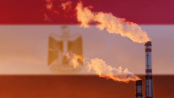 Ecological concept. Against the background of the flag of Egypt, smoke is coming from the pipes of an industrial enterprise, illustrative image. (Shutterstock) Egypt revises 2040 energy target: more gas, less renewables
