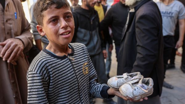 boy cries as he holds the shoes of a toddler who was killed from shrapnel following an Israeli strike