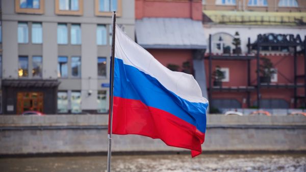 موسكو، روسيا – 6 يونيو 2025: علم روسيا على خلفية مبنى قديم يحمل كتابة "موسكو" باللغة الروسية.