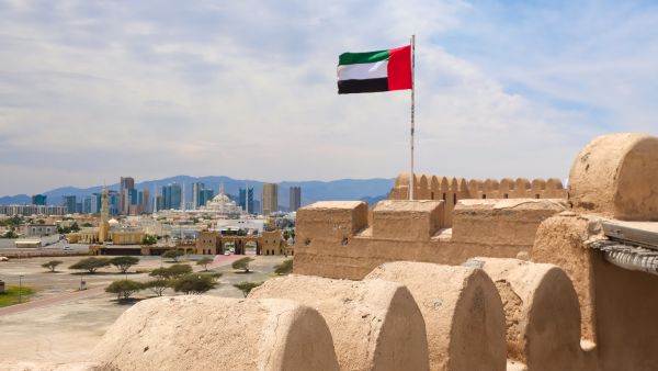 علم الإمارات العربية المتحدة يرفرف فوق قلعة الفجيرة مع أفق المدينة في الخلفية