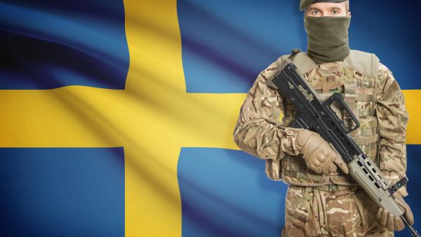 جندي يحمل بندقية رشاشة وخلفه العلم الوطني - السويد