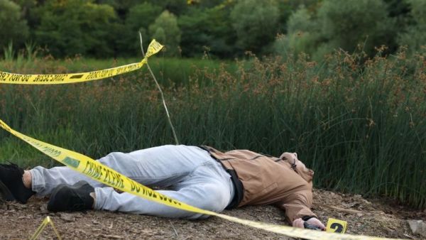 شخص ممدد على الأرض داخل موقع تحقيق جنائي محاط بشريط أمني في منطقة خارجية
