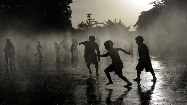أطفال يلعبون كرة القدم بينما يبردون أجسامهم في نافورة مياه، في ظل موجة حر تضرب إسبانيا