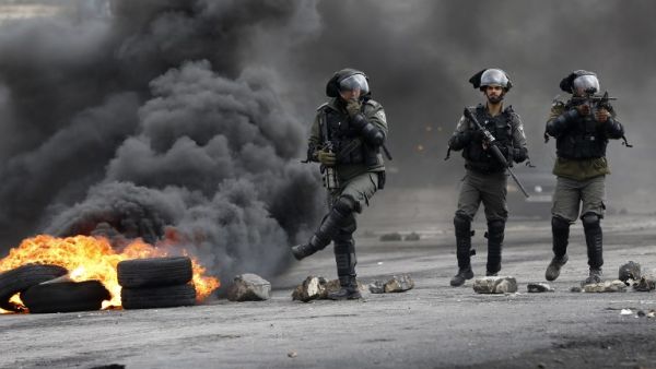 Israeli border guards walk through fumes from burning tires during clashes with Palestinian protesters near the Israeli settlement of Beit El in the Israeli occupied West Bank, on Mar. 30, 2018, after Land Day demonstrations. Land Day marks the killing of six Arab Israelis during 1976 demonstrations against Israeli confiscations of Arab land.
(ABBAS MOMANI / AFP)