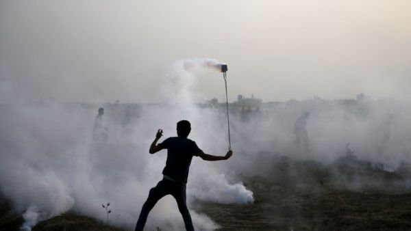 A Palestinian protester uses a slingshot in the smoke billowing from tear gas shot by Isreali forces during a demonstration along the border between Israel and the Gaza strip, east of Gaza City, on May 25, 2018. (MOHAMMED ABED / AFP)