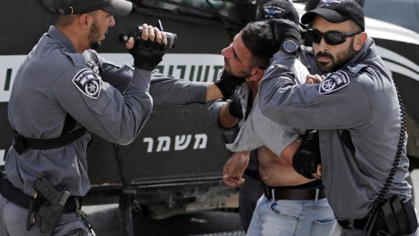 An Israeli policeman films a Palestinian as others hold him as he is being detained during a demonstration at the Palestinian Bedouin village of Khan al-Ahmar (AFP)