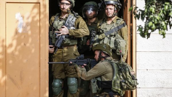 Israeli soldiers stand through a doorway as another takes aim outside during clashes with Palestinians (AFP)