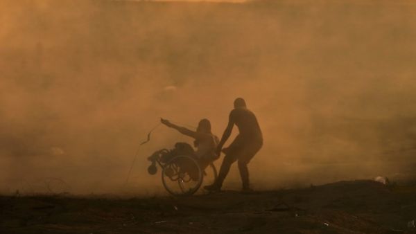 A Palestinian protester pulls a fellow protester on wheelchair amid clouds of tear gas fired by Israeli forces during clashes in east of Gaza City near the Israeli border on November 2, 2018. (MAHMUD HAMS / AFP)
