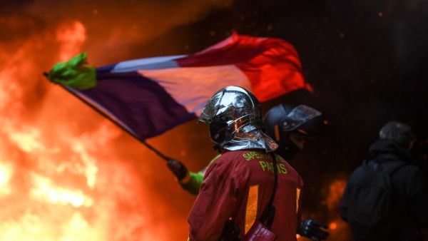 A French fire fighter walks towards flames as a Yellow vests (Gilets jaunes) demonstrator waves the French flag during protests against rising oil prices and living costs in the French capital Paris on December 1, 2018. (AFP)