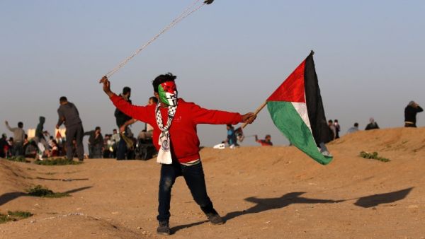 A young Palestinian protester, wearing a Guy Fawkes mask painted in the colours of the Palestinian flag and holding a Palestinian flag in his hand, uses a slingshot to hurl objects during clashes in Gaza . (AFP)