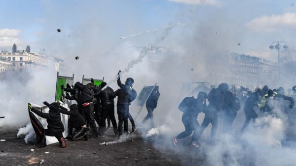 Yellow Vest protesters take shelter behind fences during clashes with riot police forces on the Champs-Elysees in Paris on March 16, 2019. (Alain JOCARD / AFP)