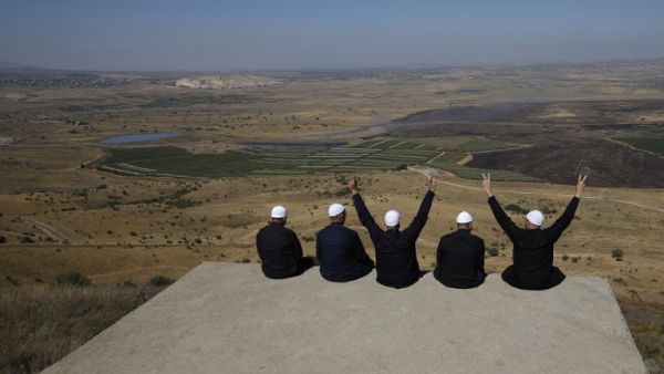 Druze men at the Israeli-annexed Golan Heights flash the V for victory sign as they look out across the southwestern Syrian province of Quneitra, visible across the border (AFP)