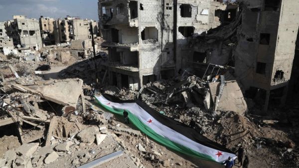 Residents and activists hold a giant a pre-Baath Syrian flag, now used by the Syrian opposition, during an anti-regime protest in the rubble of destroyed buildings in the neighborhood of Jobar, on the eastern outskirts of the capital Damascus, on March 3, 2016. (AFP/Amer Almohibany)