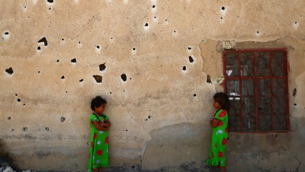 Syrian girls pose for a photograph against a bullet-riddled wall in the rebel-held village of Kafr Ghan, in the northern countryside of Aleppo, on August 28, 2017. (AFP)