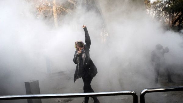 An Iranian woman raises her fist amid the smoke of tear gas at the University of Tehran during a protest driven by anger over economic problems in the capital Tehran on Dec. 30, 2017 (STR / AFP)
