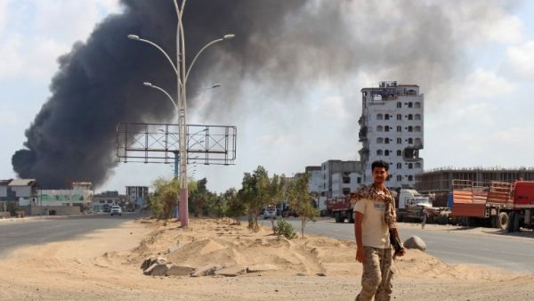 A fighters from the separatist Southern Transitional Council walks with smoke billowing in the background in the government's de facto capital Aden, as they move closer to taking full control of the southern city, on January 30, 2018 (SALEH AL-OBEIDI / AFP)