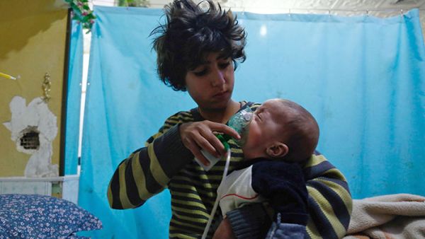 A Syrian child holds a gasmask to an infant's face in a makeshift hospital in Eastern Ghouta following a gas attack (AFP/FILE)