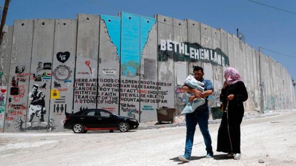 A Palestinian family walk past new graffiti painted on Israel's controversial separation barrier (AFP/File Photo)