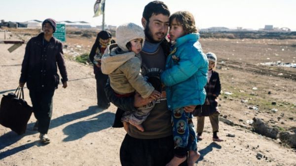 An Iraqi man carries his children near the town of Bartella as people return to their liberated neighbourhoods in eastern Mosul on January 7, 2017, (AFP)