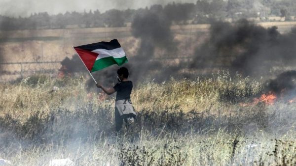 A Palestinian boy holds his national flag during clashes with Israeli security forces on the Gaza-Israel border (AFP/File Photo)	