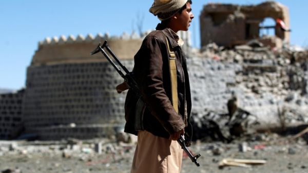 An armed Yemeni youth looks at the debris following a reported air strike in southern Sanaa. (AFP | MOHAMMED HUWAIS)
