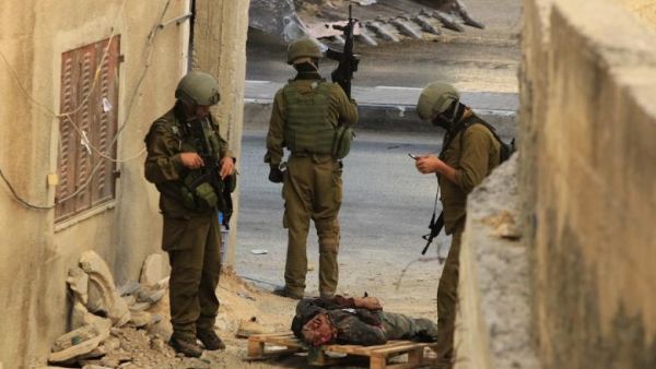 Israeli occupation forces stand over the body of a Palestinian they shot dead in the southern West Bank. (AFP/ File)