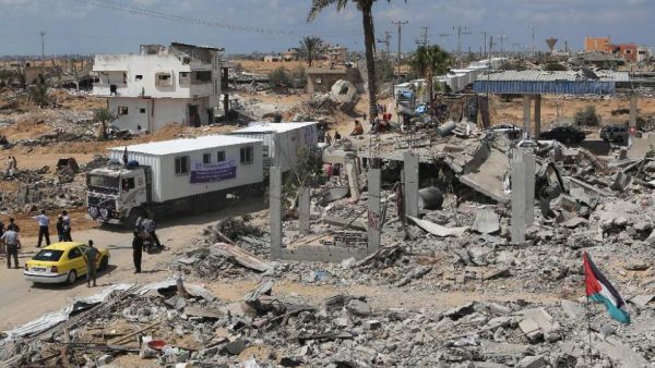 Trucks carrying mobile homes donated by Emirati charity Human Appeal International pass destroyed buildings in Khan Yunis' Khuzaa neighborhood in southern Gaza on September 13, 2014. (AFP/Said Khatib)
