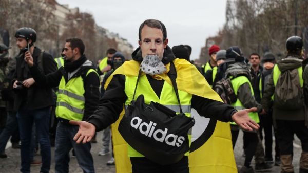 A protestor wearing a "yellow vest" (gilet jaune) and with a French President Emmanuel Macron mask poses on the Champs Elysees avenue in Paris (AFP)