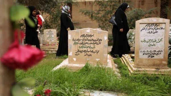 Iraqi women walk past the tomb of two unidentified Arab fighters buried in the Martyrs Cemetery of Baghdad. (AFP PHOTO/PATRICK BAZ)