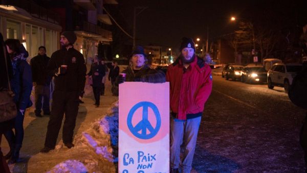 People stand with a peaceful sign near the Québec City Islamic cultural center after a shooting occurred in the mosque on Sainte-Foy Street in Quebec city on January 29, 2017. (AFP/Alice Chiche)