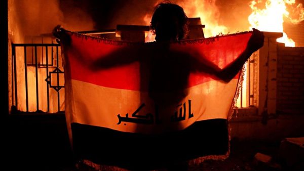 Man holding a national flag while demonstrators burn municipal complex (Twitter)