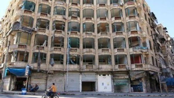 رجل يستقل دراجة نارية بجوار مبنى تعرضت واجهته لدمار في حلب
