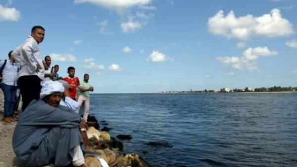 مصريون يجلسون على شاطئ قرية رشيد يراقبون مركبا انطلق في عملية بحث عن عشرات المفقودين في كارثة غرق مركب كان يقل مهاجرين
