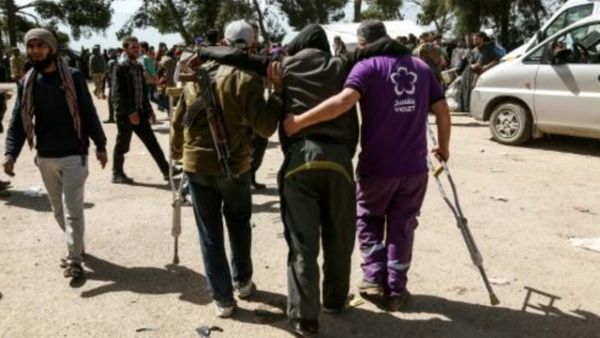 مقاتل من المعارضة السورية يحمل رشاشه فيما يساعد متطوع جريحا عند وصولهما الى قلعة المضيق بعد عملية الاجلاء من الغوطة الشرقية

