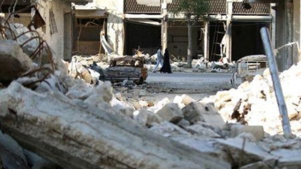 أشخاص يمشون بجوار مبنى مدمر في منطقة محاصرة تسيطر عليها المعارضة في حلب بسوريا
