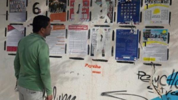 تونسي ينظر إلى ملصقات عليها قوائم المرشحين للانتخابات البلدية المرتقبة في القصرين بوسط تونس
