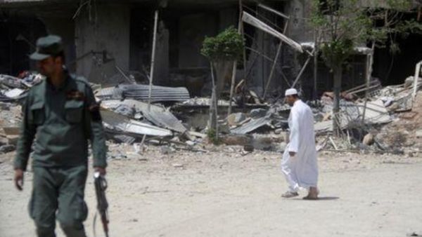 جندي من الجيش السوري يقف ممسكا بسلاحه ورجل يمر من أمام مبان مهدمة في مدينة دوما بدمشق في سوريا يوم الجمعة

