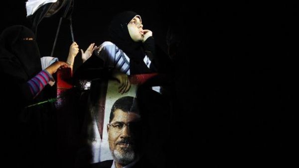 An Egyptian supporter of the Muslim Brotherhood holds the portraits of deposed president Mohamed Morsi during a rally outside Cairo's Rabaa al-Adawiya mosque late on July 7, 2013. [AFP]