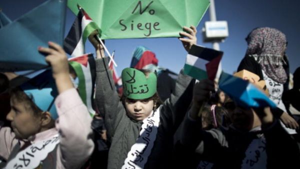 A Palestinian child raises up a paper ship reading 'No siege' during a rally to protest against the Israeli siege of the Gaza Strip on November 30, 2013 at Gaza City harbour. [Mahmud Hams/AFP]