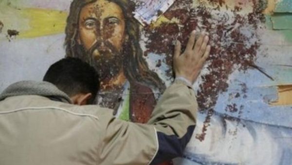مسيحي قبطي يقف امام لوحة للمسيح عند كنيسة القديسين لطختها الدماء