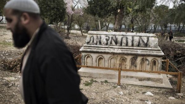 A Muslim man walks past a tomb vandalised with spray paint with a graffiti reading in Hebrew: “Mohammed (prophet) is Dead” at the Mamun Allah cemetery, an old Muslim cemetery in Jerusalem. (AFP/File) 