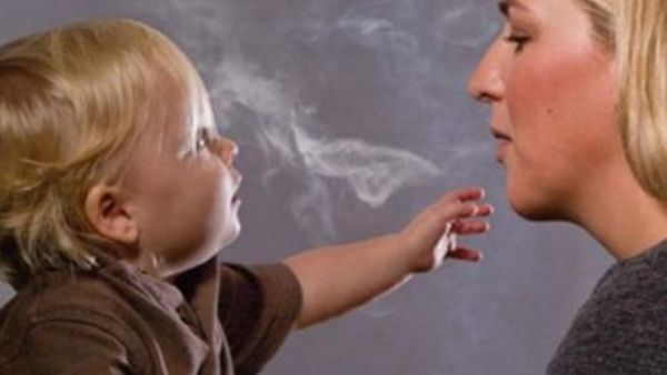 صورة تعبيرية لأم تنفث الدخان في وجه طفلها وتعرضه للخطر 