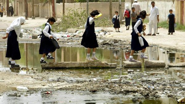 Young school girls cross a trash ridden patch of water on stones in the middle of the road on their way home in Basra. (AFP/ File)