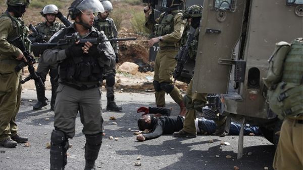Israeli soldiers stand over an injured Palestinian man during clashes near Ramallah in the West Bank, October 7, 2015. (AFP/File)